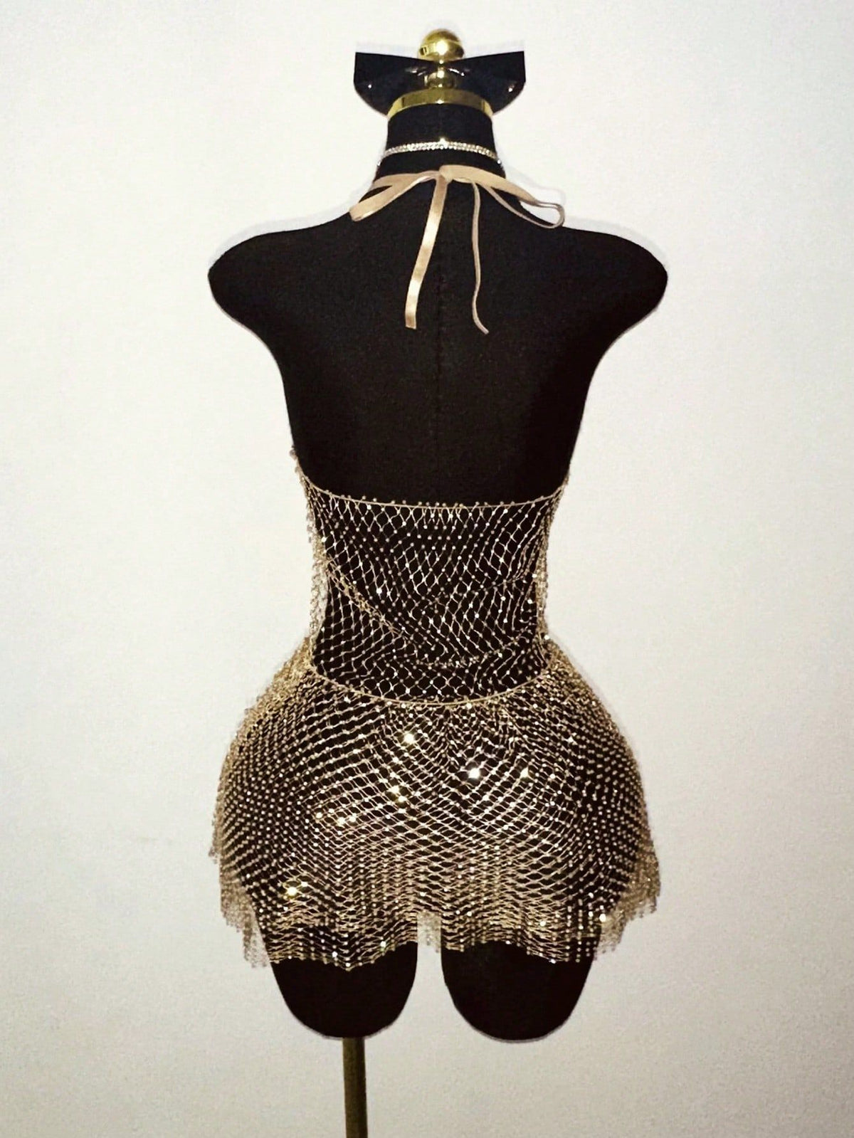 Warm-toned rhinestone halter mini dress with mesh fringe hem on a mannequin