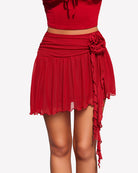 Red mesh mini skirt with ruched waist and side drape tied to the hem, rosette detail.
