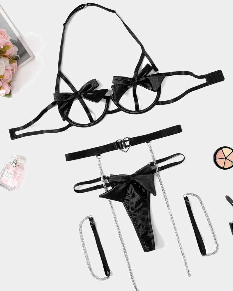 Black bow lingerie set flat lay: bra, belt, thong, and chain garters