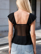 Back of black sheer mesh top showing square neckline, flutter sleeves, and transparent panel
