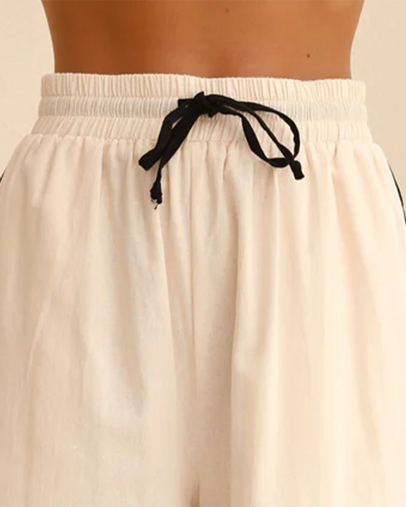 Beige linen pajama shorts with elastic waist and black drawstring bow.