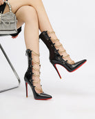 Black patent stiletto ankle boots with gold chain wrap and red sole.