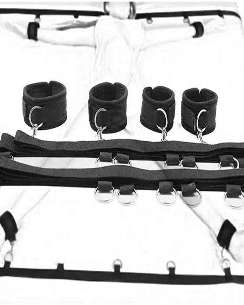 Black wrist and ankle cuffs with metal rings attached to padded straps on bed