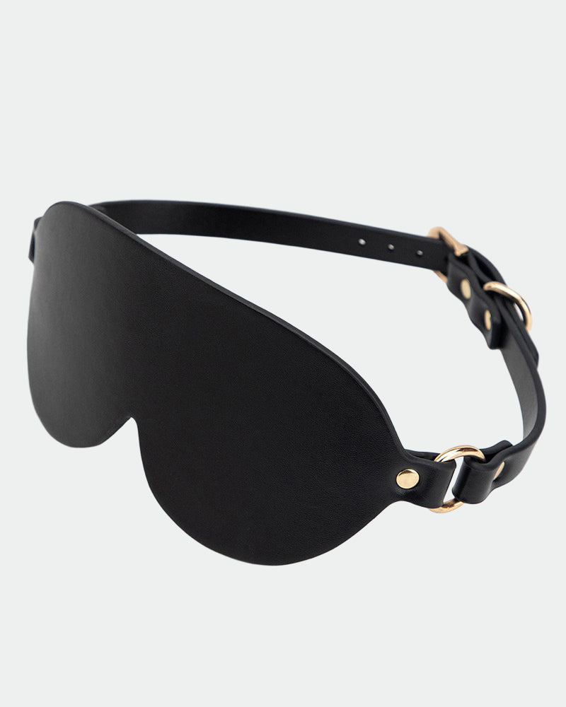 Black leather eye mask with curved eye cup shape and adjustable strap with metal rings