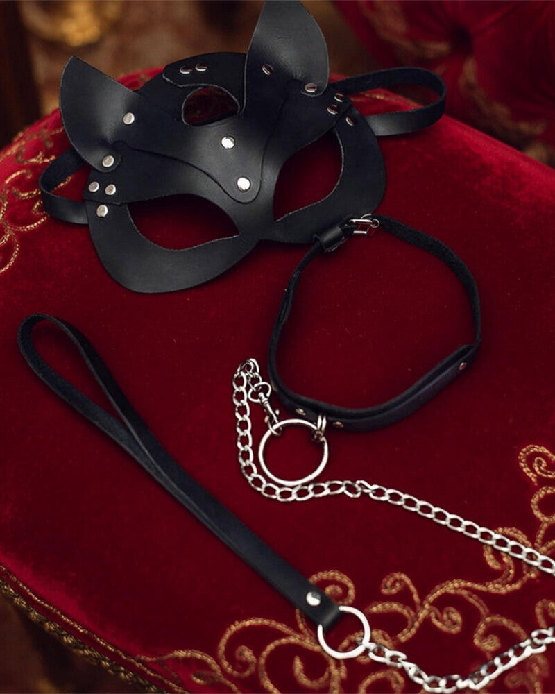 Black leather cat mask with ear cutouts and stud accents, with matching leash on red cloth