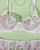 Close-up of white heart-embroidered lace underwire bra with scalloped trim and mesh cups.