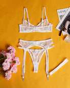 White sheer lace lingerie set flat lay: underwire bra, thong, and garter straps.