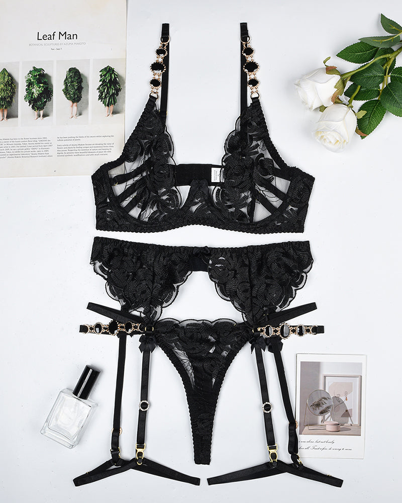 Black lace lingerie set laid flat: bra, garter belt, and thong with straps