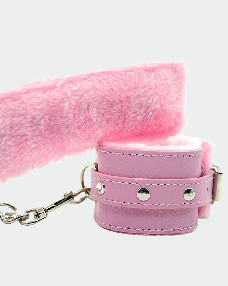 Pink leather plush wrist cuff close-up with metal ring, studs, and fastening strap