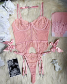 Pink lace lingerie set flat lay: corset, thong, garters, bows, and matching stockings