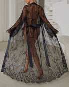 Black sheer lace robe dress with satin belt, open back, long draped sleeves.