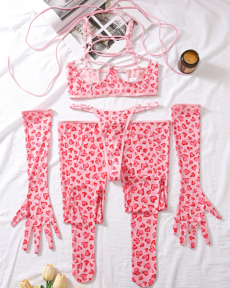 Pink heart-pattern lingerie set laid flat: lace-up mesh bra, thong, and long leg socks