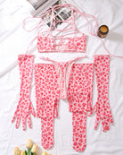 Pink heart-pattern lingerie set laid flat: mesh bra, tie-front thong, arm warmers, leg socks