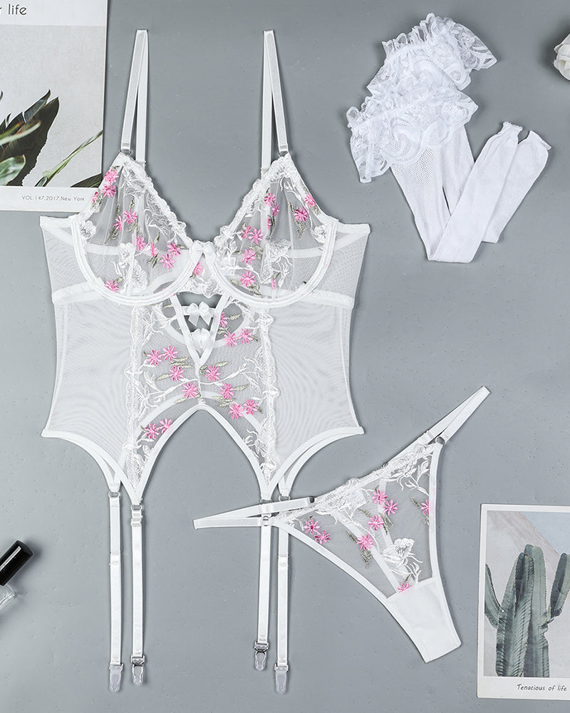 White floral-embroidered lingerie set flat lay with bra, bodysuit, thong, garters, and stockings