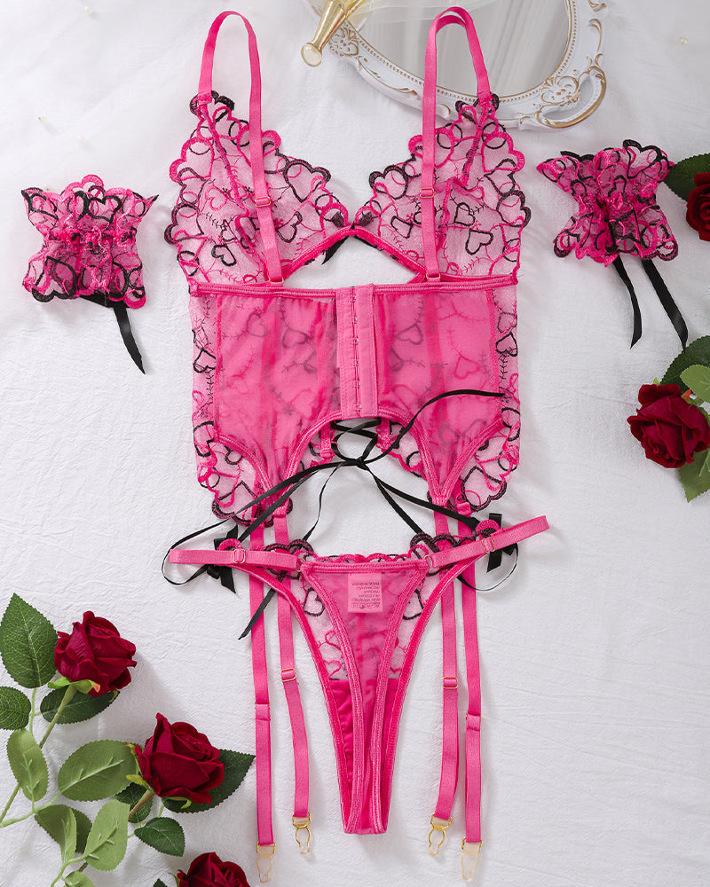 Pink heart embroidered lingerie set on flat lay with strappy bra, corset front, and garter straps