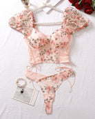 Pink embroidered bra and thong set with ruffled sleeves and lace-up trim, flat lay