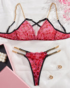 Red sheer lace bra and thong set with black trim; gold chain accessories laid flat