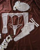 White lingerie set pieces: bodysuit, garter belt, stockings, gloves and thong, flat lay