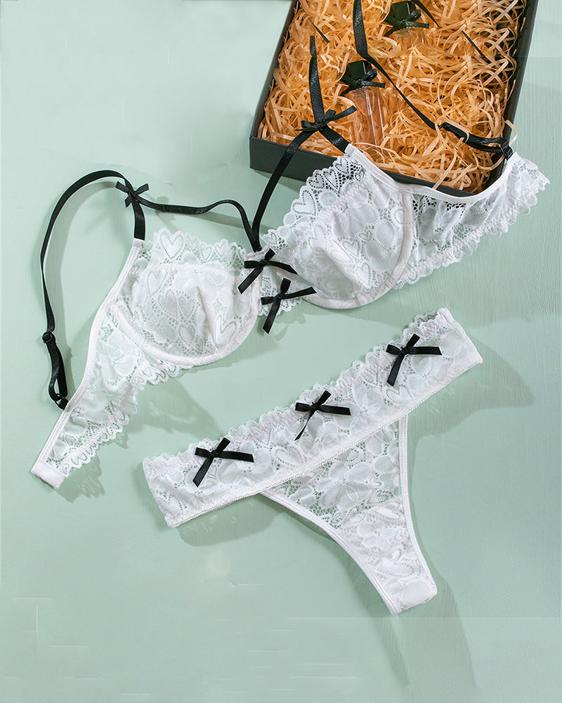 White lace bra and panty set with black bow trim laid flat