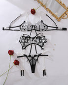 Flat lay of black sheer heart-embroidered lingerie set: bra, thong, garter straps
