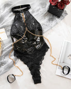 Black lace and vinyl-look halter bodysuit laid flat with gold chain accessories