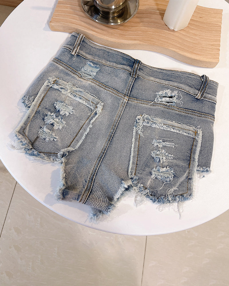Blue high-waisted distressed denim shorts laid flat with two ripped back patches and fray