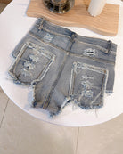 Blue high-waisted distressed denim shorts laid flat with two ripped back patches and fray