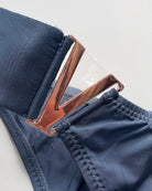 Close-up of copper-tone V metal hardware on a blue thong waistband.