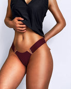 Maroon thong panties with copper-tone V metal accents at the sides, minimal coverage.