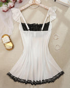 White satin babydoll mini dress with black lace bodice, thin straps, and lace hem