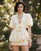 Champagne pleated mini dress with deep V neckline, puff sleeves, and floral waist rosette