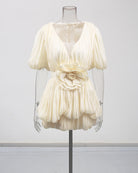 Champagne pleated mini dress with deep V, puff sleeves, and floral waist rosette