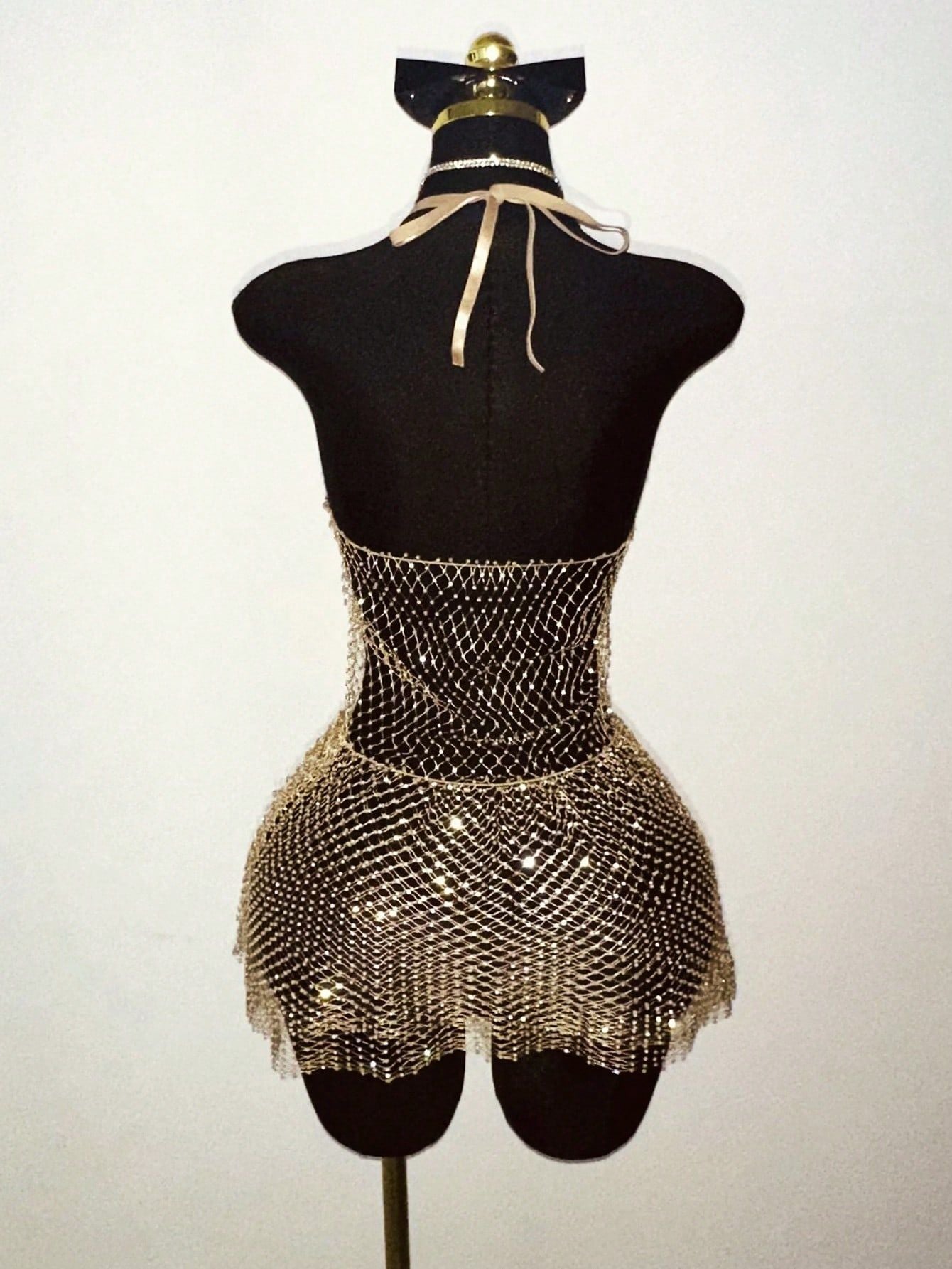 Warm-toned rhinestone halter mini dress with mesh fringe hem on a mannequin