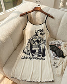 Cream spaghetti-strap mini slip dress on hanger with skull graphic and scalloped hem