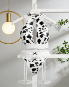 Cow print halter keyhole bra and lace panty set with garter straps, hanging on hangers