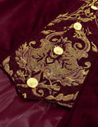 Close-up of burgundy coat cuff embroidery with gold baroque pattern and buttons